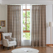 The curtains are made of a sheer, lightweight fabric with a semi-transparent quality that allows natural light to filter through. Their design features a plaid pattern in warm brown, beige, and subtle gray tones, giving them a cozy yet airy appearance.