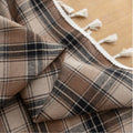 Close-up of brown, beige, and black plaid curtain fabric with a soft, textured weave and decorative white tassel trim along the edge.