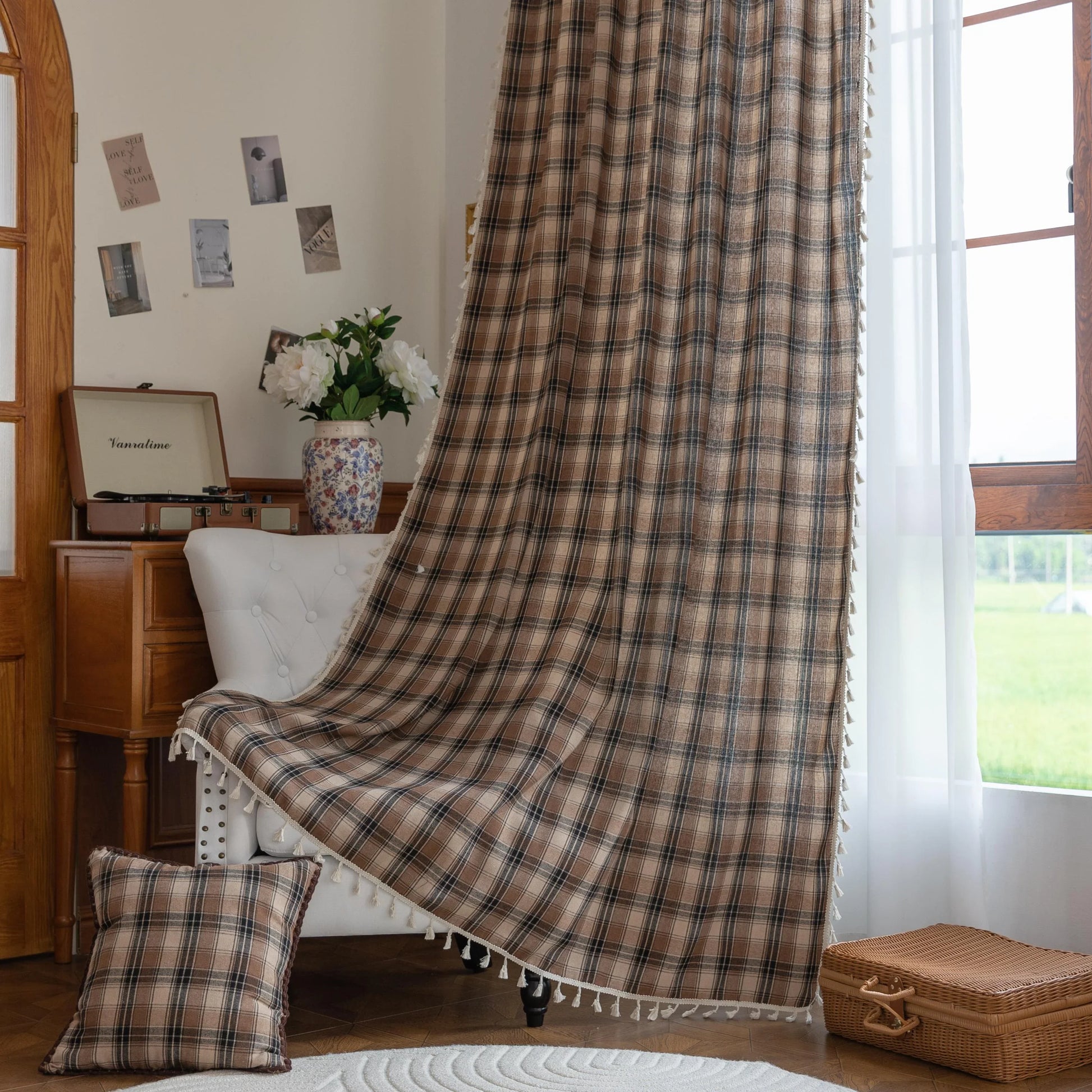 Brown, beige, and black plaid curtain fabric with a soft, textured weave and decorative white tassel trim along the edge.