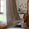 Brown, beige, and black plaid curtain fabric with a soft, textured weave and decorative white tassel trim along the edge.