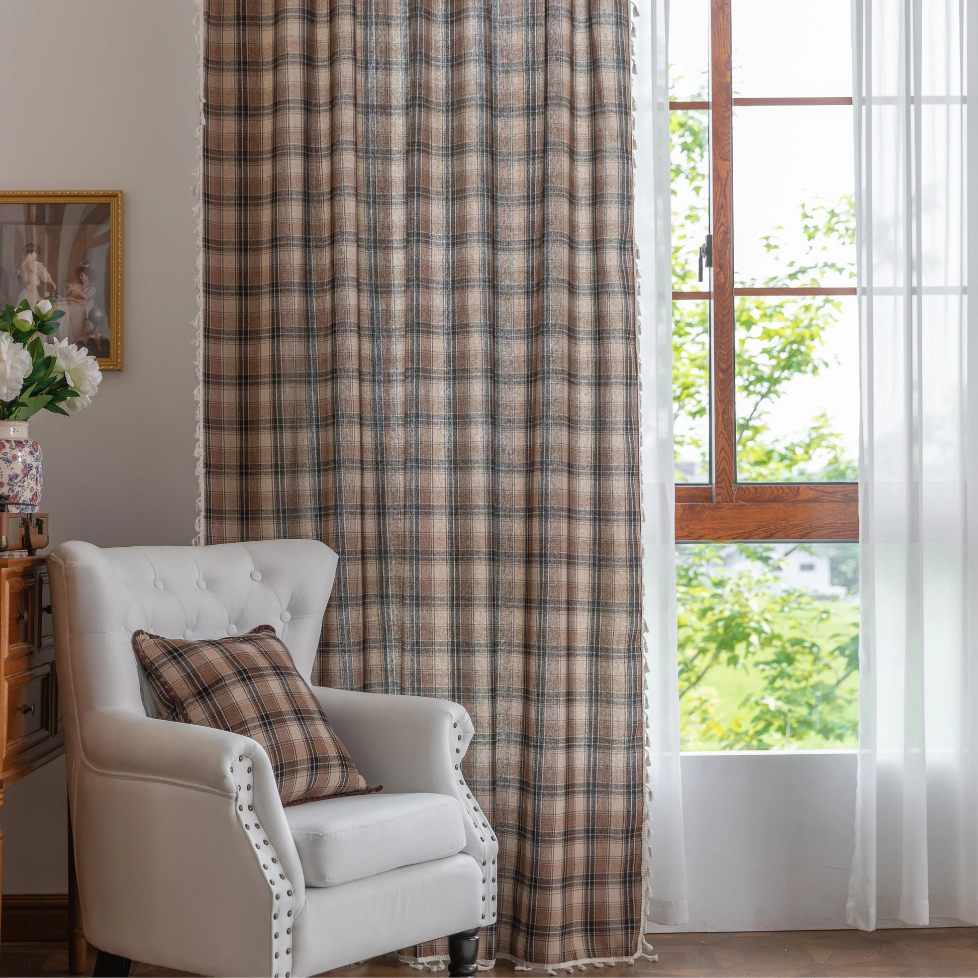 Brown, beige, and black plaid curtain fabric with a soft, textured weave and decorative white tassel trim along the edge.