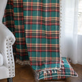 Green, red, and beige plaid curtain fabric with a soft, woven texture, finished with decorative white tassel trim along the edge.