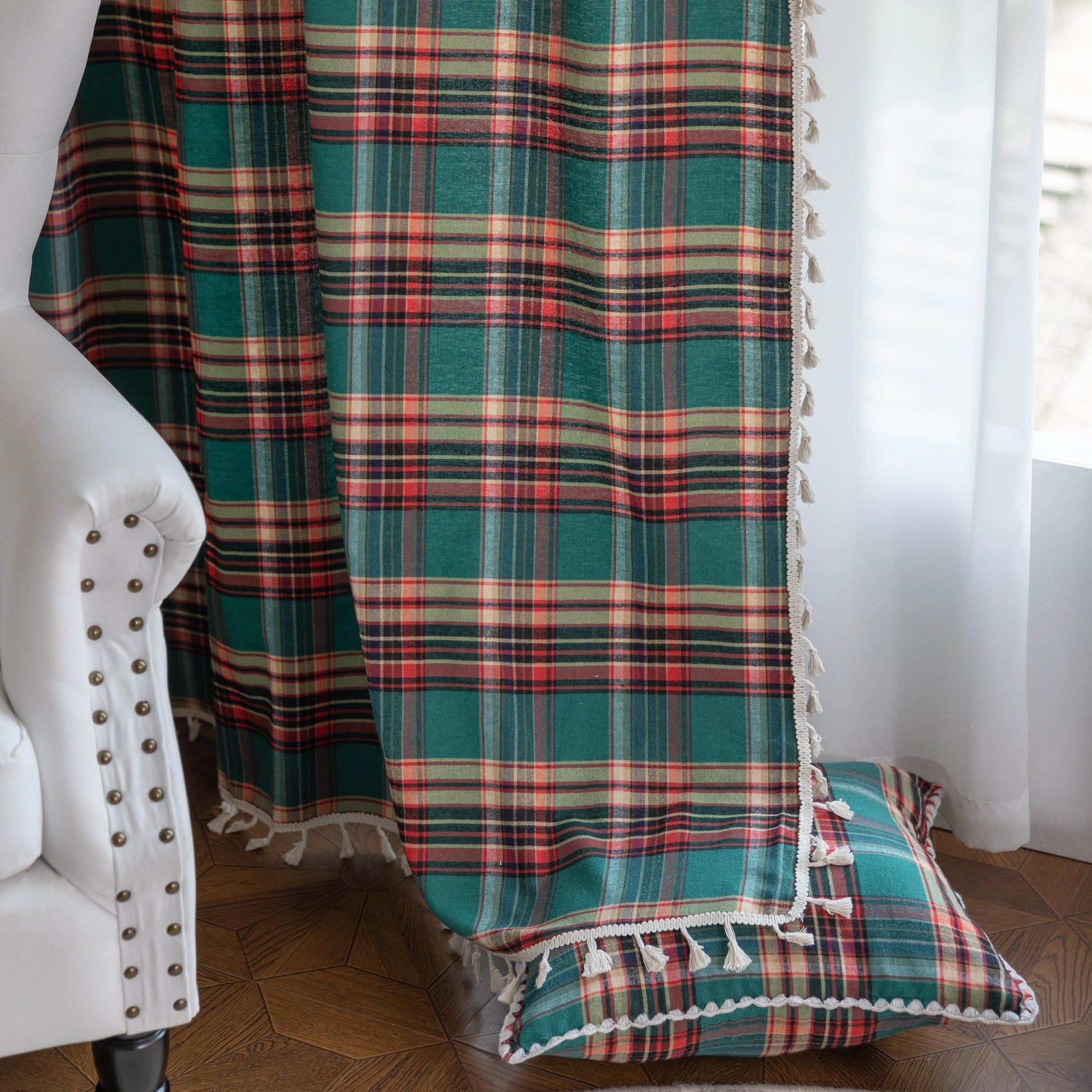 Green, red, and beige plaid curtain fabric with a soft, woven texture, finished with decorative white tassel trim along the edge.