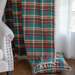 Green, red, and beige plaid curtain fabric with a soft, woven texture, finished with decorative white tassel trim along the edge.