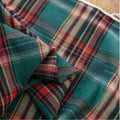 Green, red, and beige plaid curtain fabric with a soft, woven texture, finished with decorative white tassel trim along the edge.
