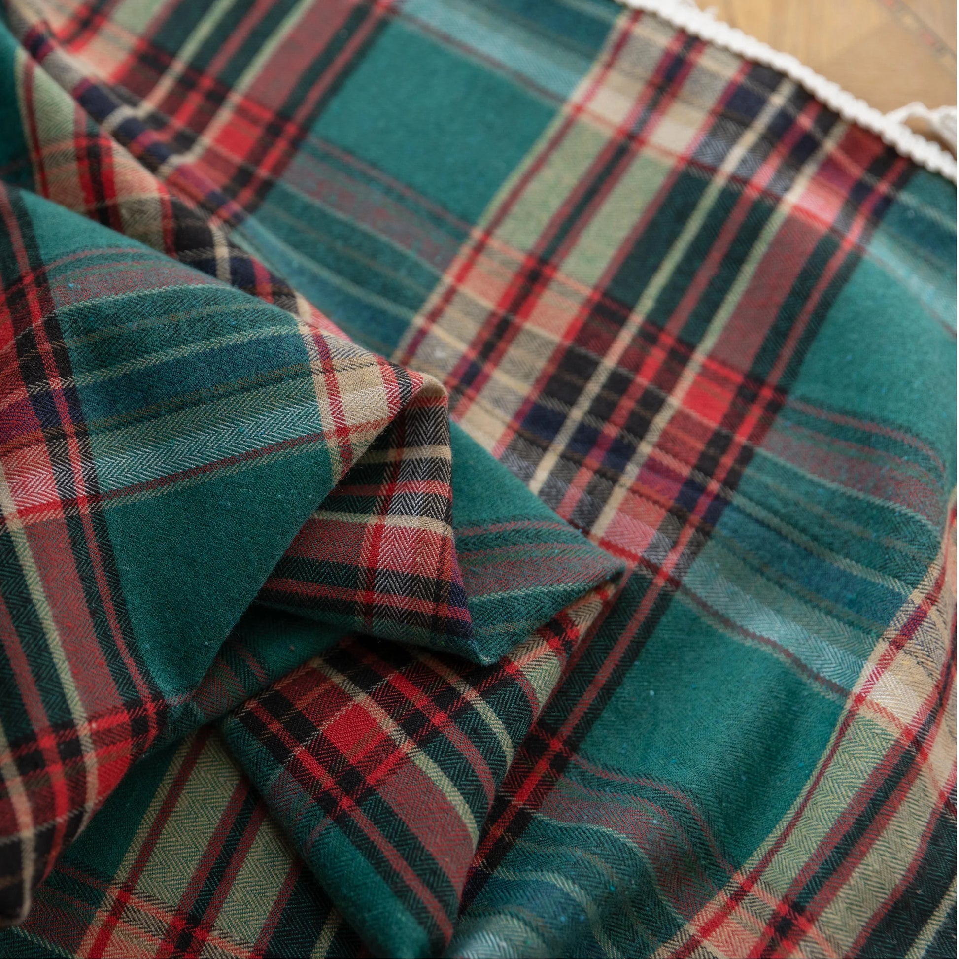 Green, red, and beige plaid curtain fabric with a soft, woven texture, finished with decorative white tassel trim along the edge.