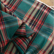 Green, red, and beige plaid curtain fabric with a soft, woven texture, finished with decorative white tassel trim along the edge.