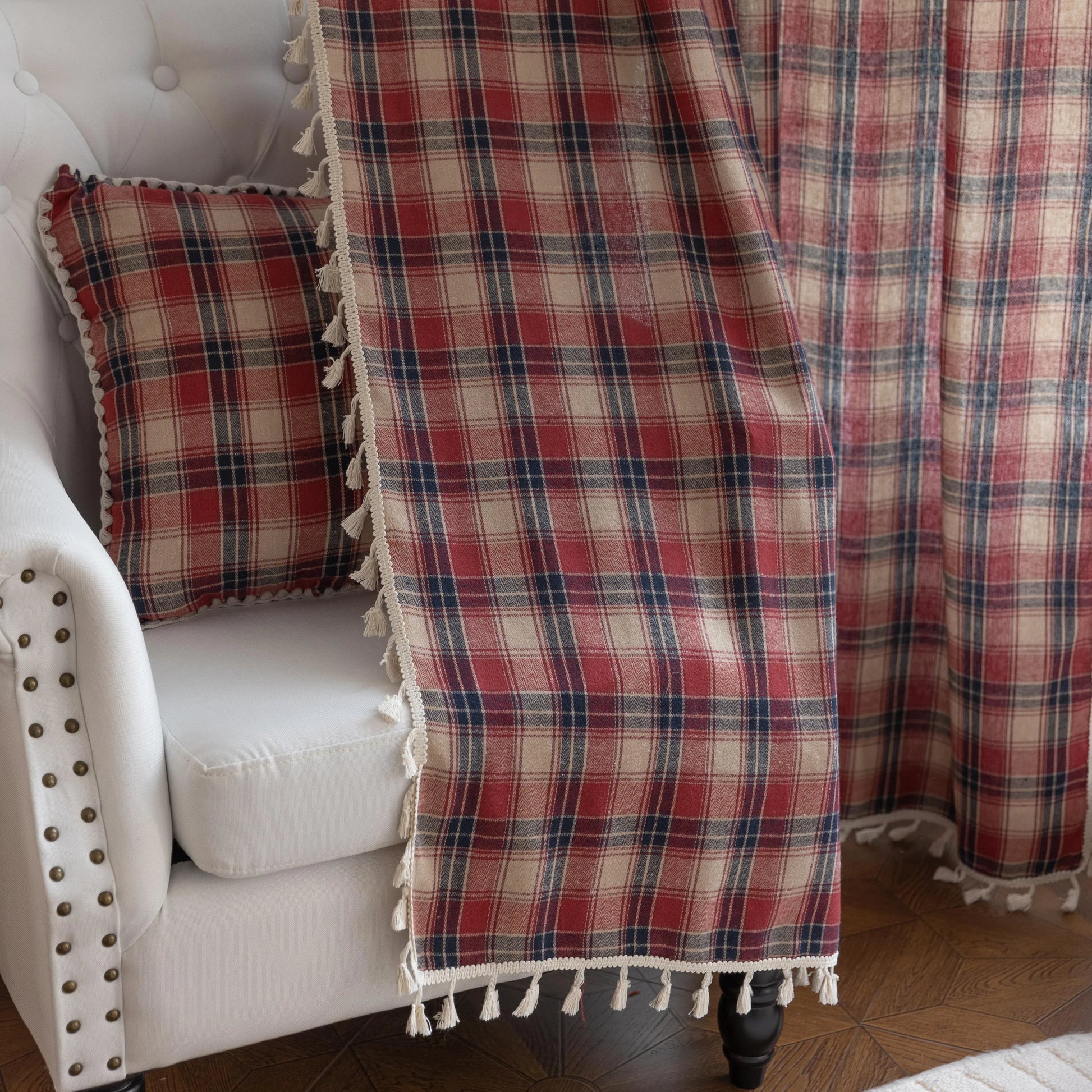 Red, navy blue, and beige plaid curtain fabric with a soft, textured weave and decorative white tassel trim on the edge.