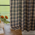 Beige and navy blue plaid curtain fabric with a soft, textured weave and decorative white tassel trim along the edge.