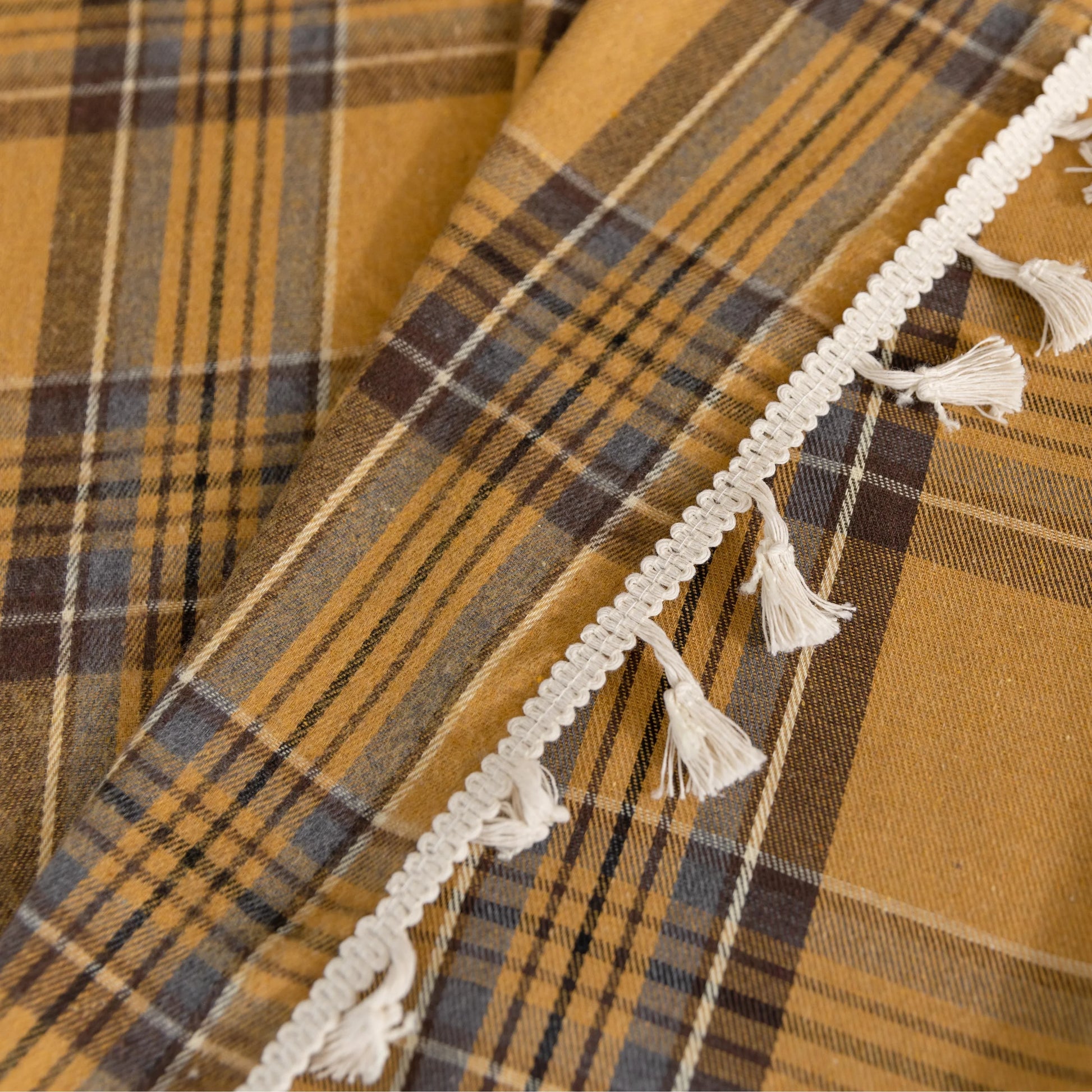 Mustard yellow and navy blue plaid curtain fabric with a soft, woven texture and decorative white tassel trim on the edge.