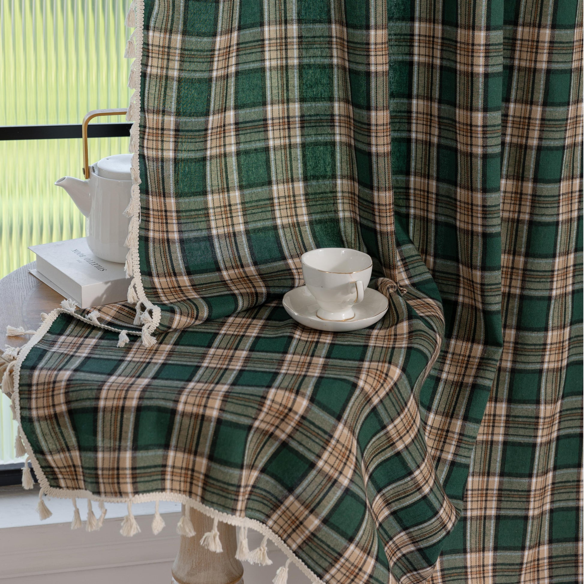 Green and beige plaid curtain fabric with a soft, woven texture, accented by decorative white tassel trim along the edge.