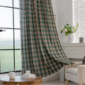 Green and beige plaid curtain fabric with a soft, woven texture, accented by decorative white tassel trim along the edge.