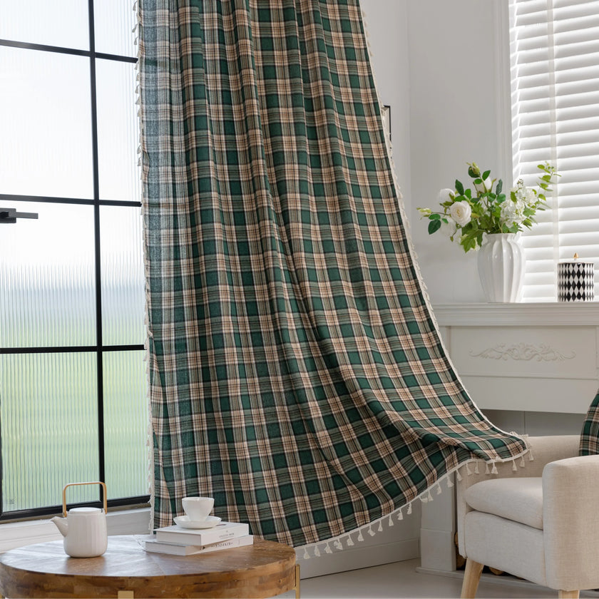 Green and beige plaid curtain fabric with a soft, woven texture, accented by decorative white tassel trim along the edge.