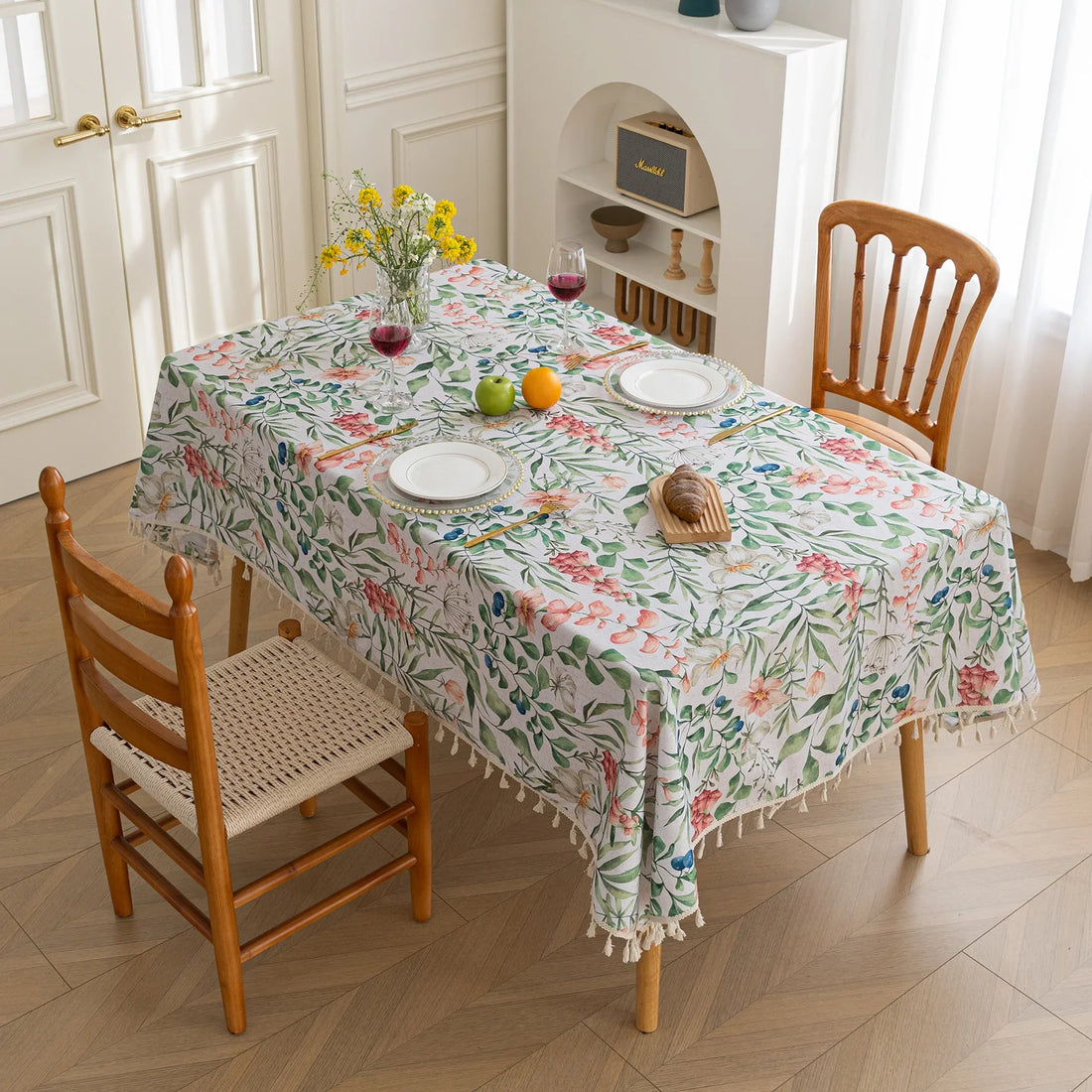 Elegant floral tablecloth with lush green leaves and soft pastel blossoms, accented by delicate tassel edging — perfect for adding a fresh, nature-inspired touch to dining rooms, garden parties, or spring gatherings.