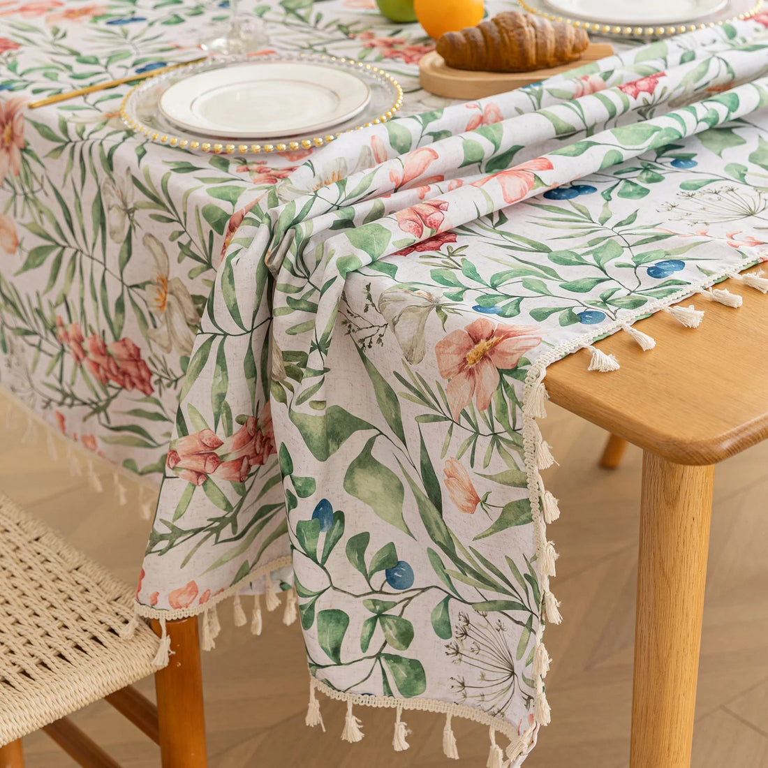 Elegant floral tablecloth with lush green leaves and soft pastel blossoms, accented by delicate tassel edging — perfect for adding a fresh, nature-inspired touch to dining rooms, garden parties, or spring gatherings.