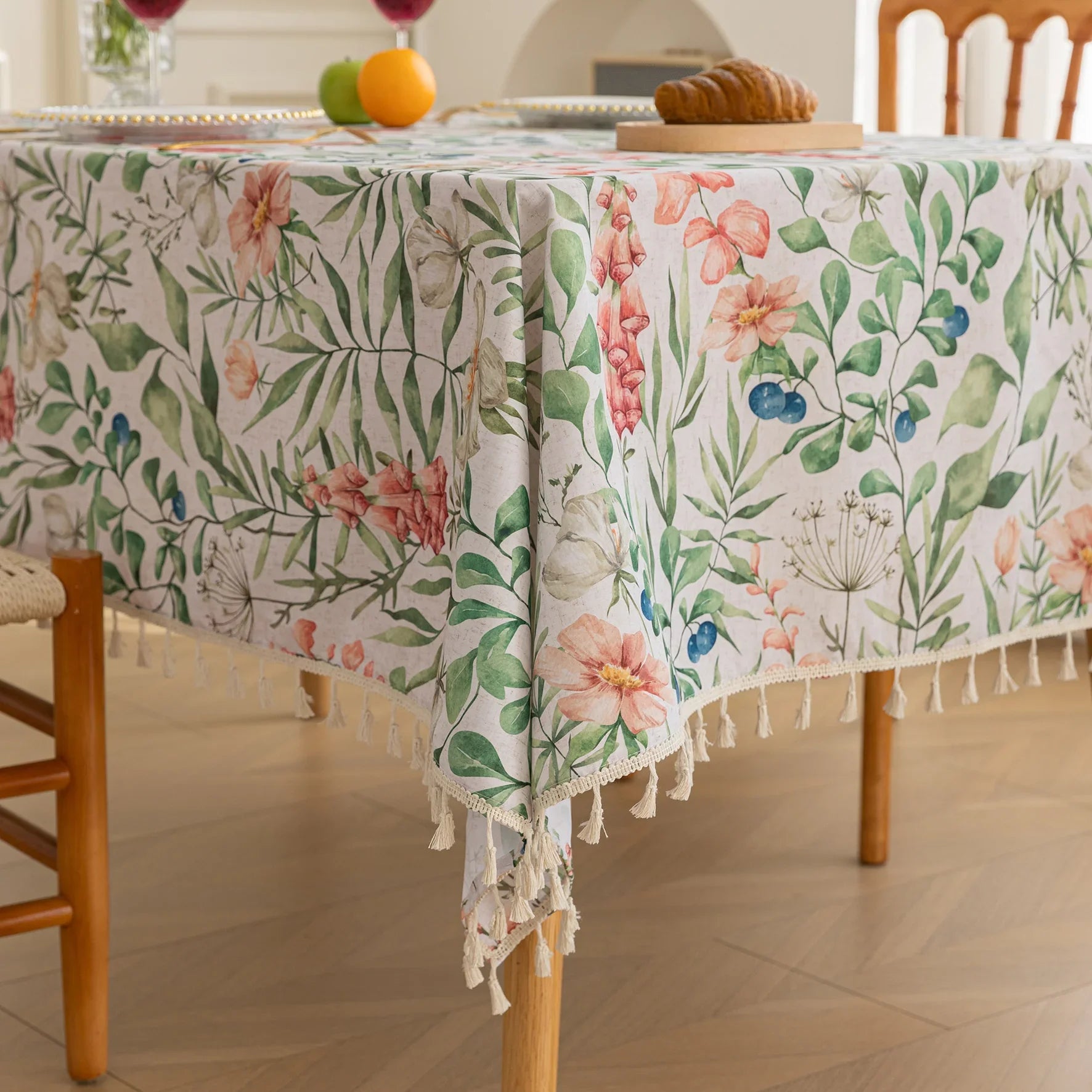 Elegant floral tablecloth with lush green leaves and soft pastel blossoms, accented by delicate tassel edging — perfect for adding a fresh, nature-inspired touch to dining rooms, garden parties, or spring gatherings.