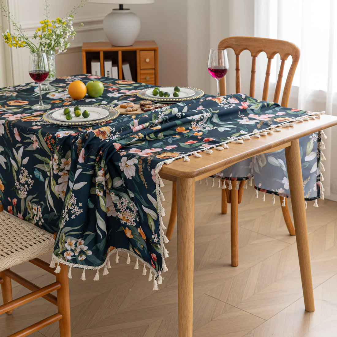 Chic dark floral tablecloth featuring vibrant botanical prints on a deep navy background, finished with elegant tassel edges — ideal for elevating dining décor, special occasions, and stylish everyday meals.