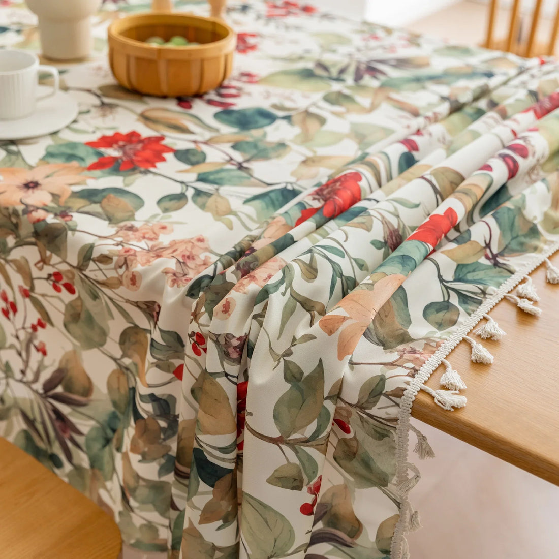 Beautiful floral tablecloth with vibrant red, green, and beige botanical patterns, enhanced by delicate tassel edging — perfect for adding a warm, inviting touch to everyday dining or festive gatherings.
