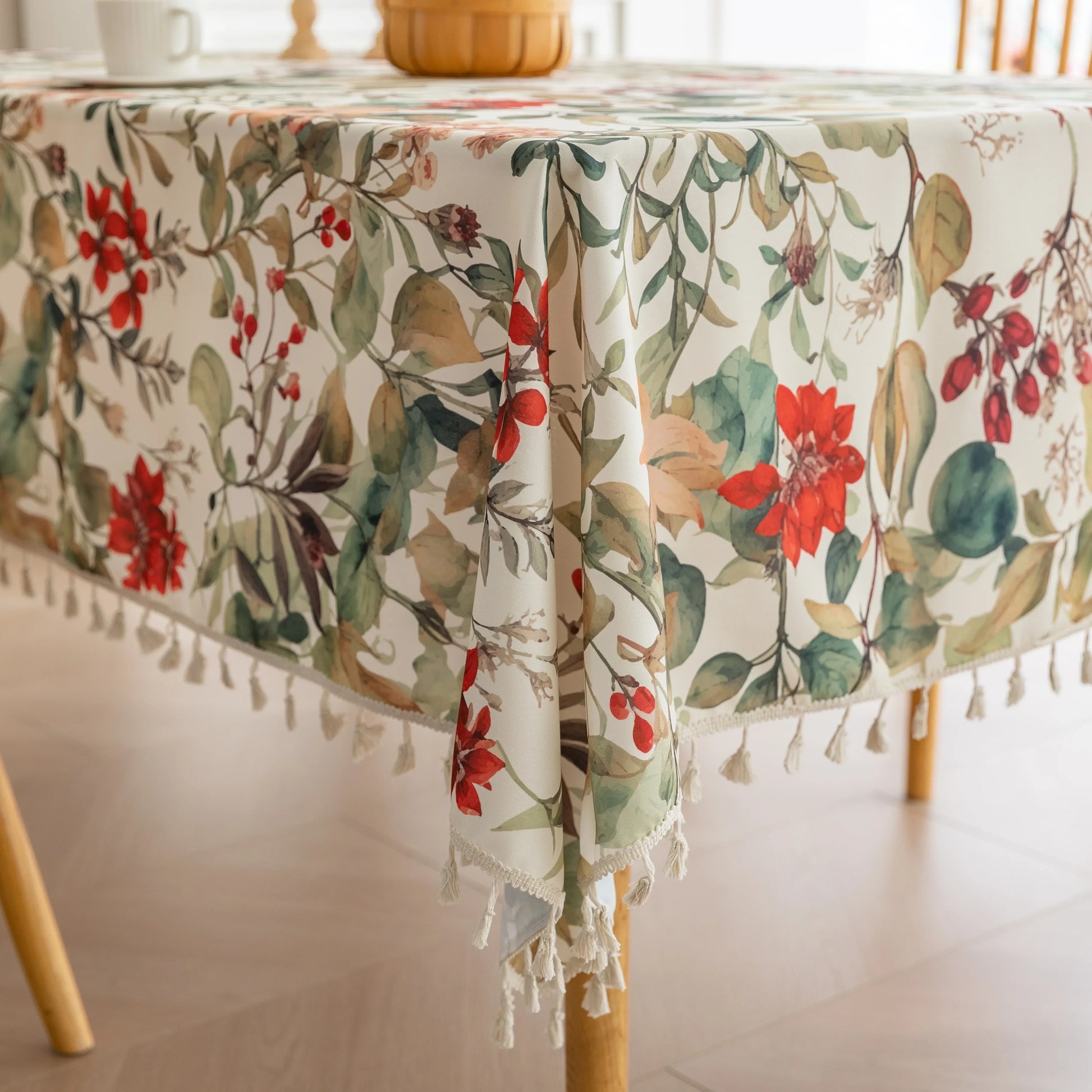 Beautiful floral tablecloth with vibrant red, green, and beige botanical patterns, enhanced by delicate tassel edging — perfect for adding a warm, inviting touch to everyday dining or festive gatherings.