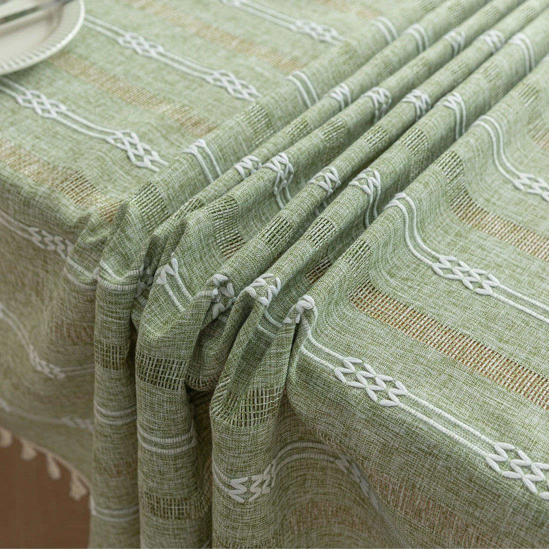 Light green woven tablecloth with white geometric stripe patterns and decorative tassel edges.