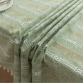 Light green woven tablecloth with white geometric stripe patterns and decorative tassel edges.