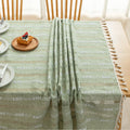 Light green woven tablecloth with white geometric stripe patterns and decorative tassel edges.