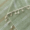 Light green woven tablecloth with white geometric stripe patterns and decorative tassel edges.