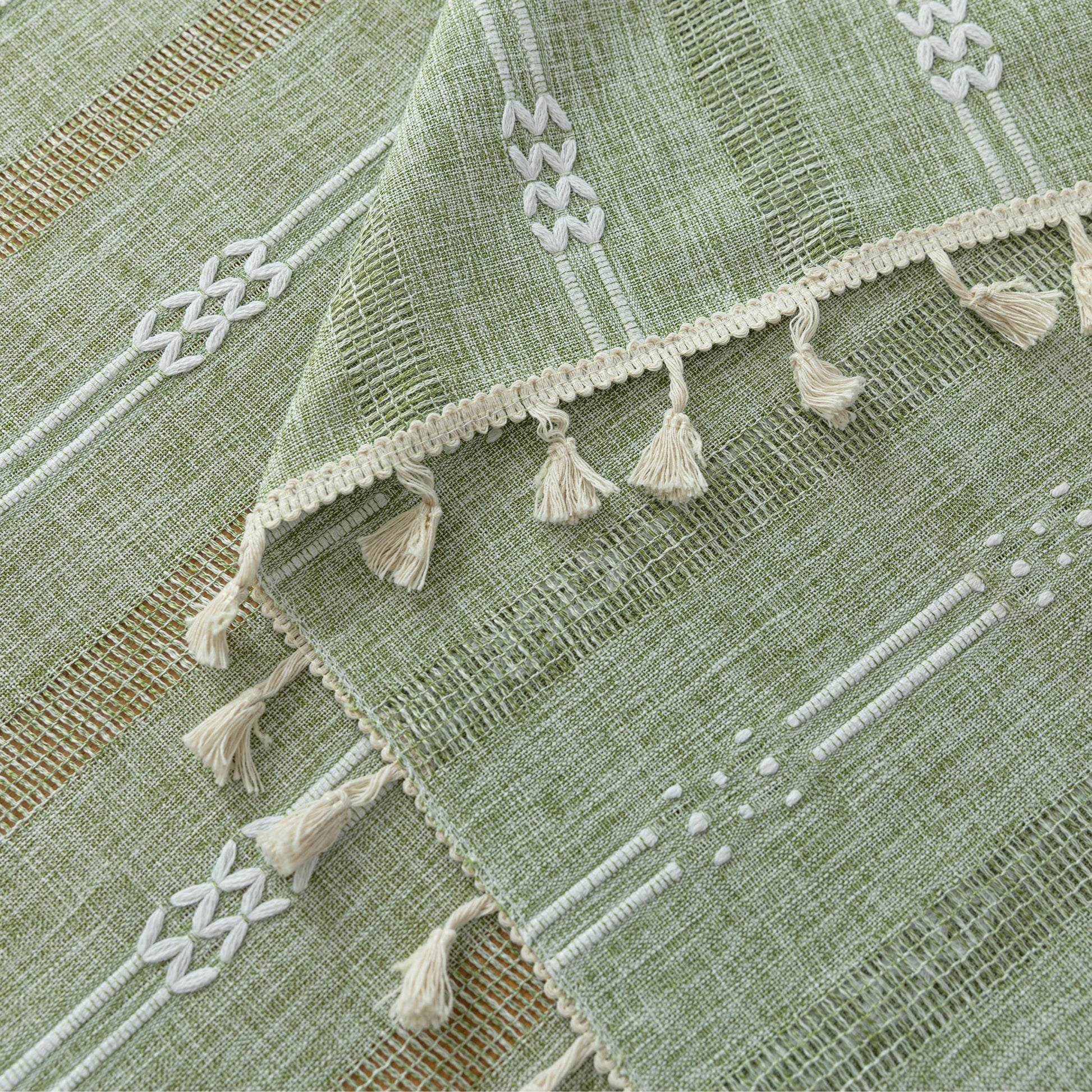 Light green woven tablecloth with white geometric stripe patterns and decorative tassel edges.