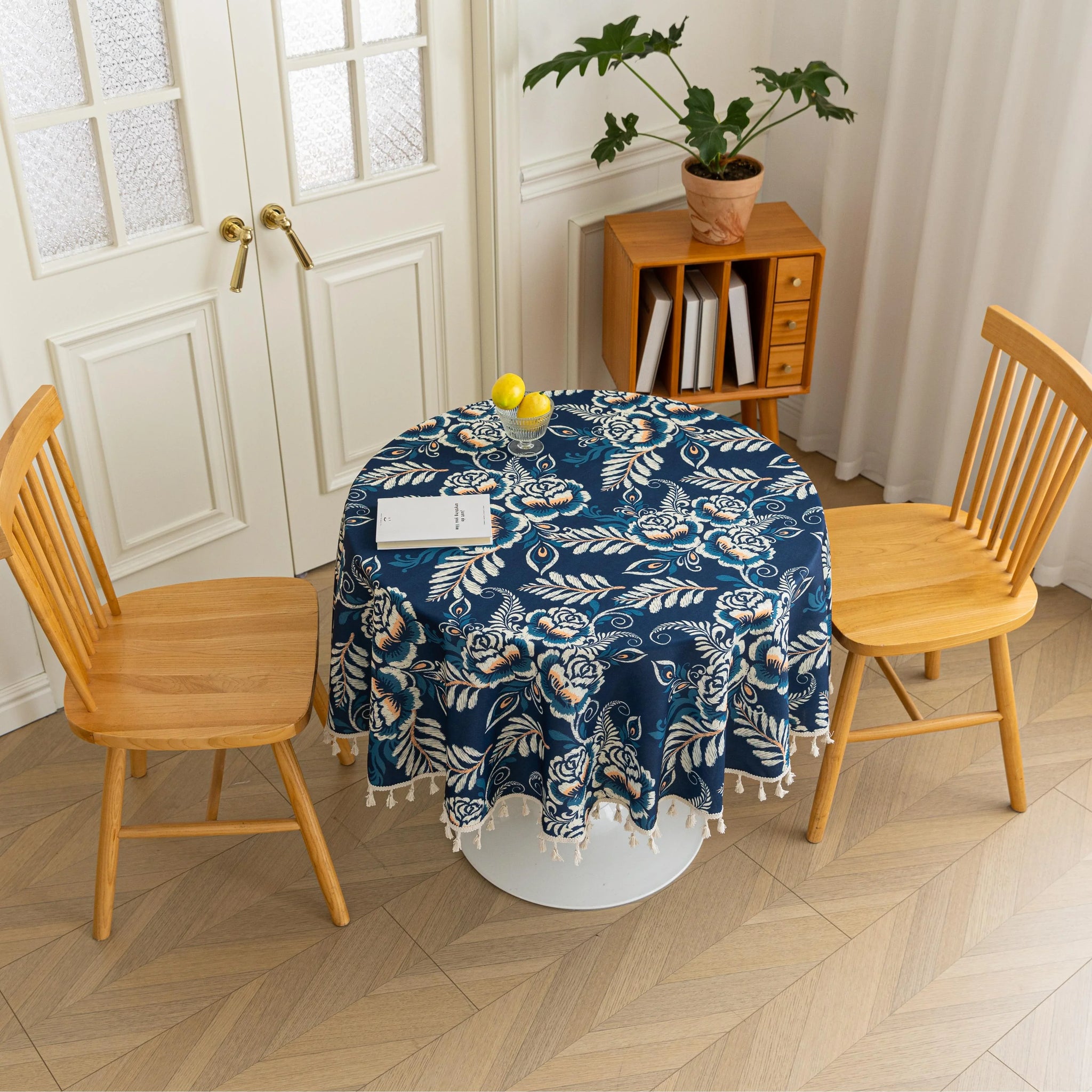Elegant Floral Round Tablecloth – Enhance your dining space with this stylish round tablecloth featuring a deep navy blue background adorned with delicate white and beige floral patterns. Accented with charming white tassels along the edge, it brings a refined yet cozy touch to your table décor. Perfect for everyday meals, afternoon tea, or special gatherings, this durable and decorative tablecloth suits both modern and classic interiors.
