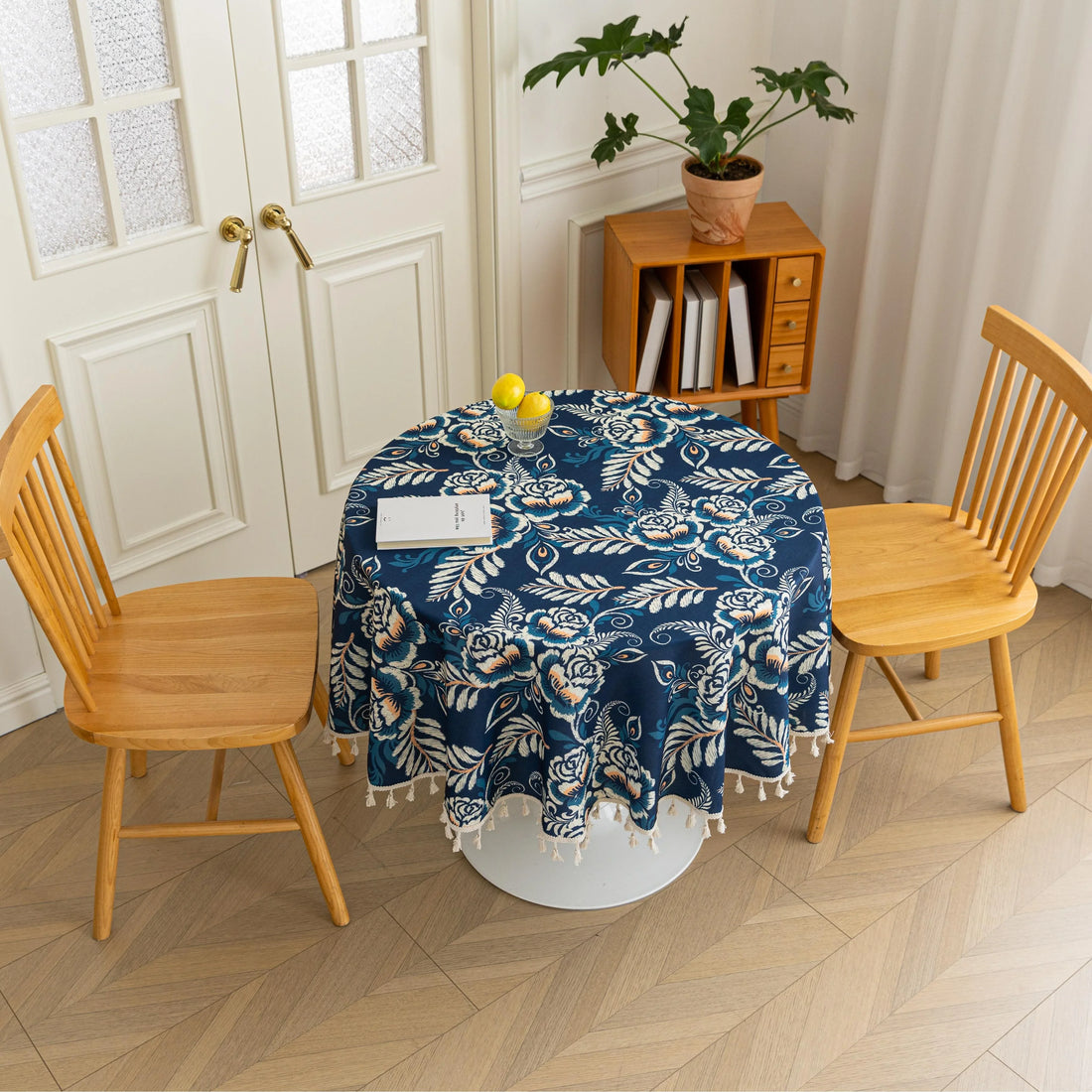 Elegant Floral Round Tablecloth – Enhance your dining space with this stylish round tablecloth featuring a deep navy blue background adorned with delicate white and beige floral patterns. Accented with charming white tassels along the edge, it brings a refined yet cozy touch to your table décor. Perfect for everyday meals, afternoon tea, or special gatherings, this durable and decorative tablecloth suits both modern and classic interiors.
