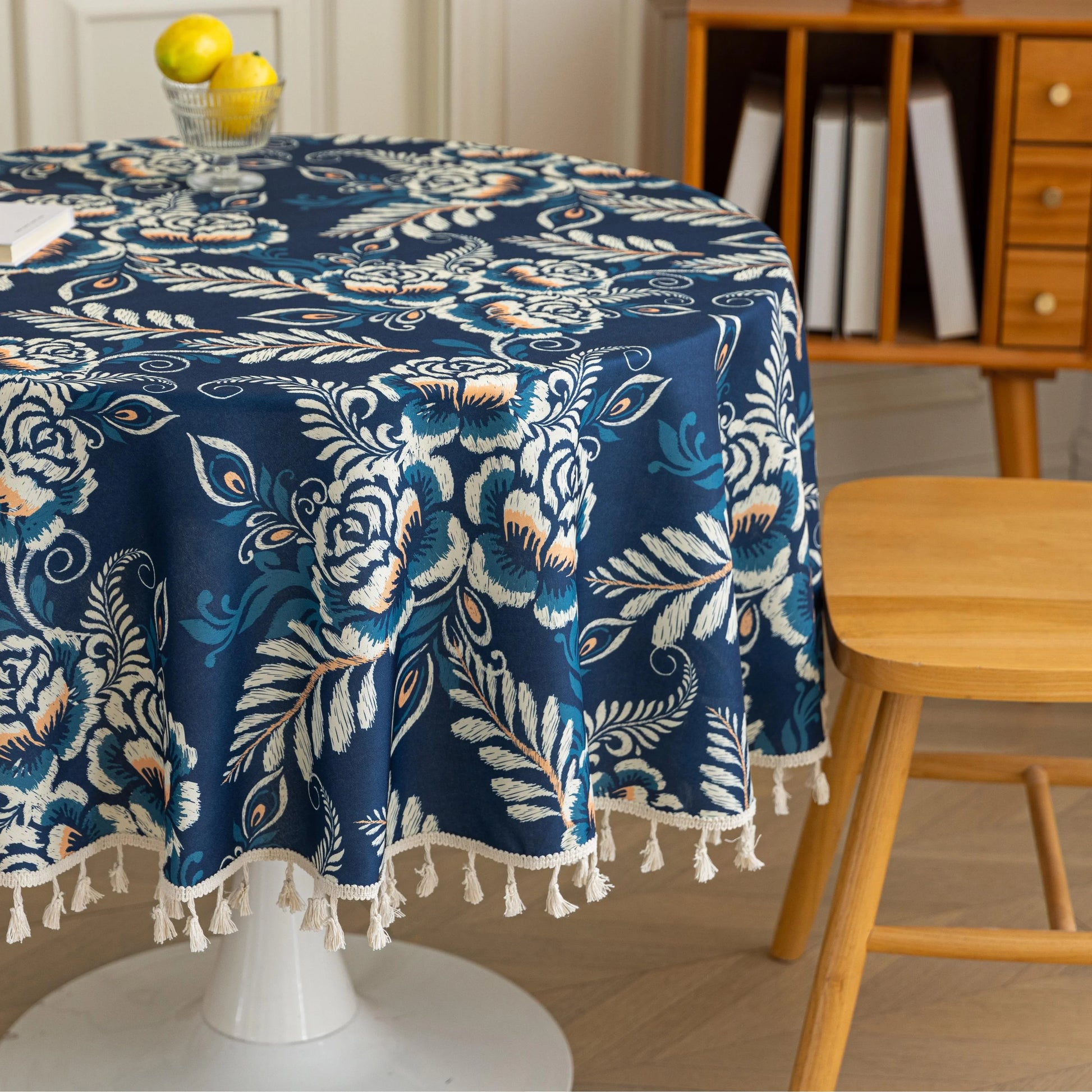 Elegant Floral Round Tablecloth – Enhance your dining space with this stylish round tablecloth featuring a deep navy blue background adorned with delicate white and beige floral patterns. Accented with charming white tassels along the edge, it brings a refined yet cozy touch to your table décor. Perfect for everyday meals, afternoon tea, or special gatherings, this durable and decorative tablecloth suits both modern and classic interiors.
