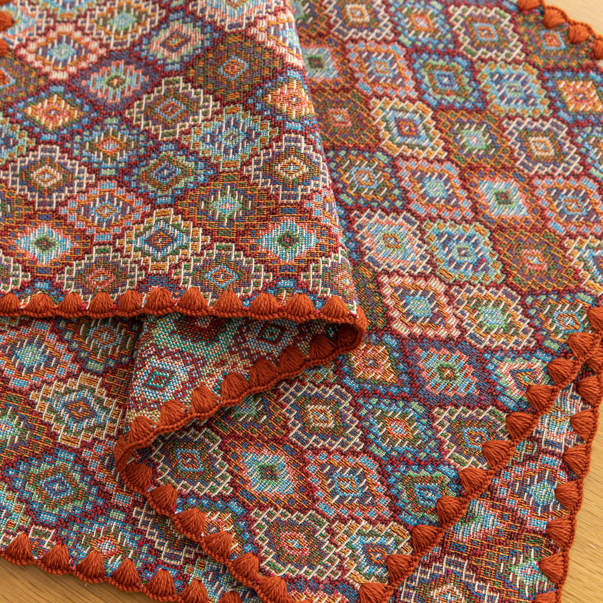 Colorful woven placemat with intricate diamond patterns, adding a vibrant boho touch while protecting your dining table.